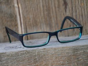 Lesebrille aus Celluloseacetat, auf einem Holzbalken liegend, vor einer Holzwand.