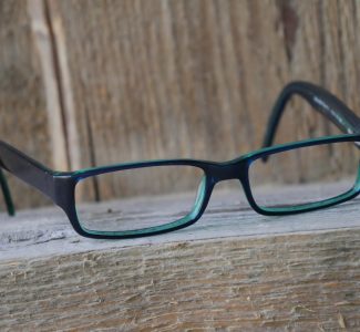 Lesebrille aus Celluloseacetat, auf einem Holzbalken liegend, vor einer Holzwand.