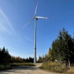 Windenergieanlage im Wald gesäumt von Nadelbäumen.