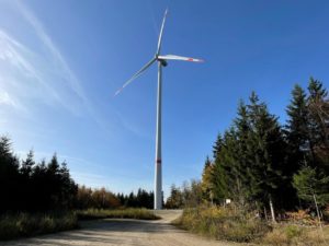 Windenergieanlage im Wald gesäumt von Nadelbäumen.