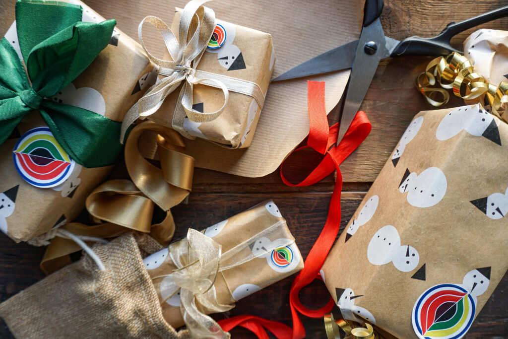 Schere mit Geschenkband und viele in Kraftpapier verpackt Geschenke liegen auf einem Tisch.