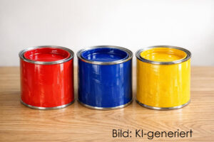Drei Farbdosen in rot, blau und gelb stehen auf einem Holzbrett.